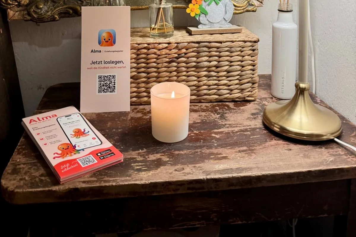 Alma-Aufsteller mit QR-Code und Flyern auf einem Holztisch neben einer Kerze